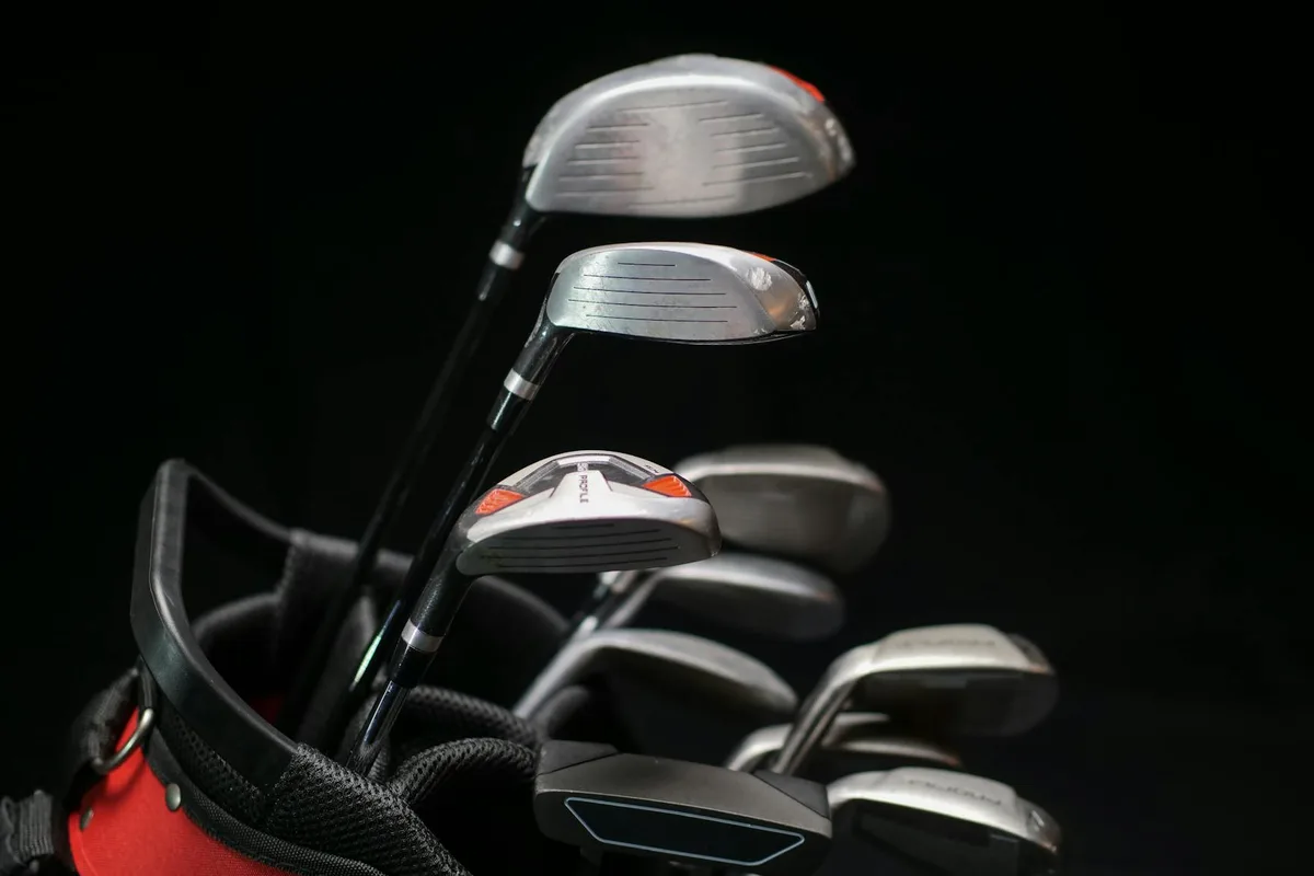 A set of golf irons, woods, and a putter laid out on a course showing different club types