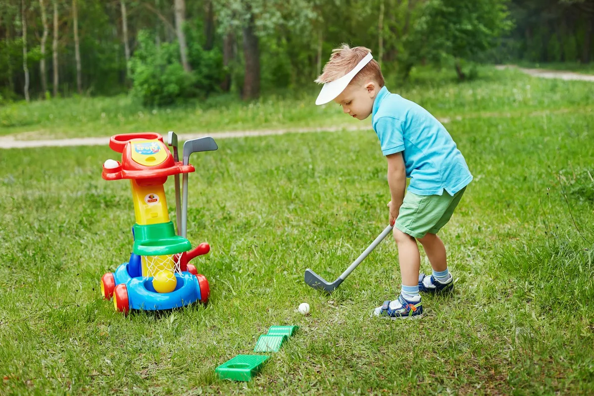 A young golfer smiling and holding a junior golf club at the edge of a practice green