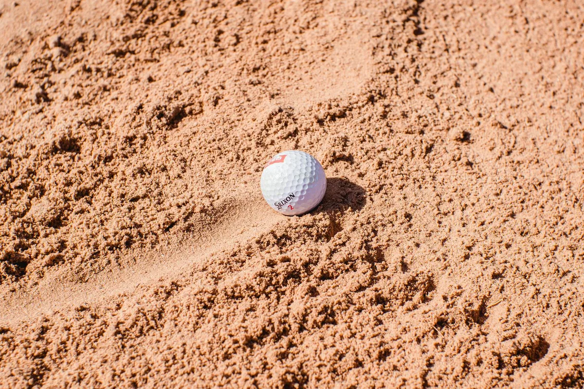 A golfer playing a sand shot from a greenside bunker with a spray of sand