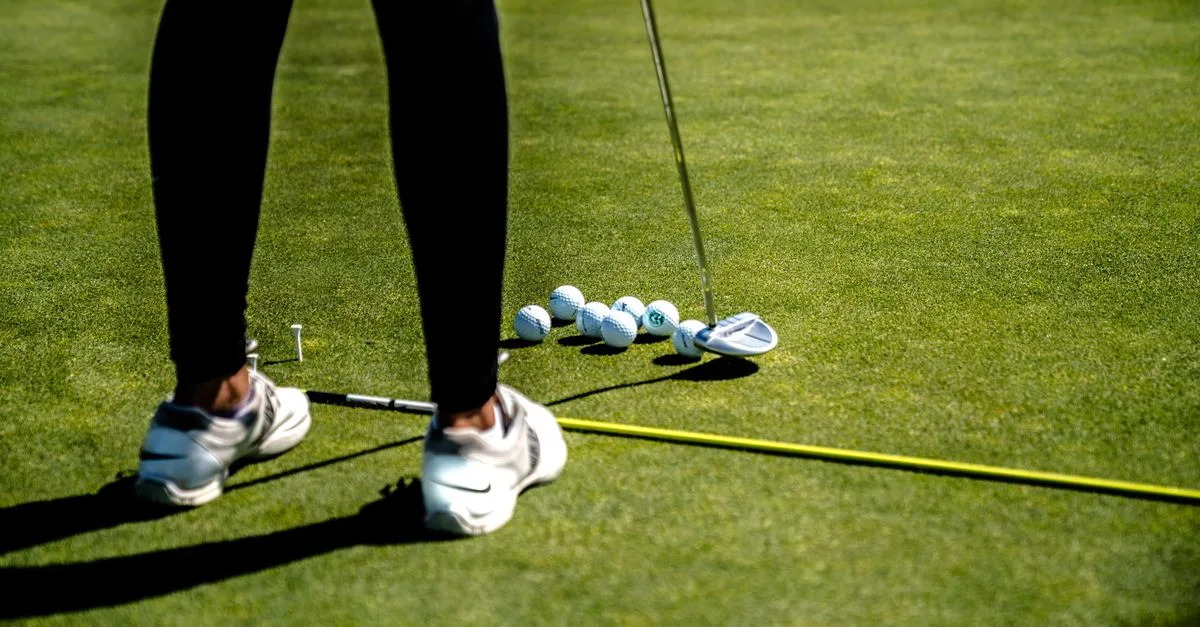 A golfer crouching to study the line of a putt on a manicured putting green