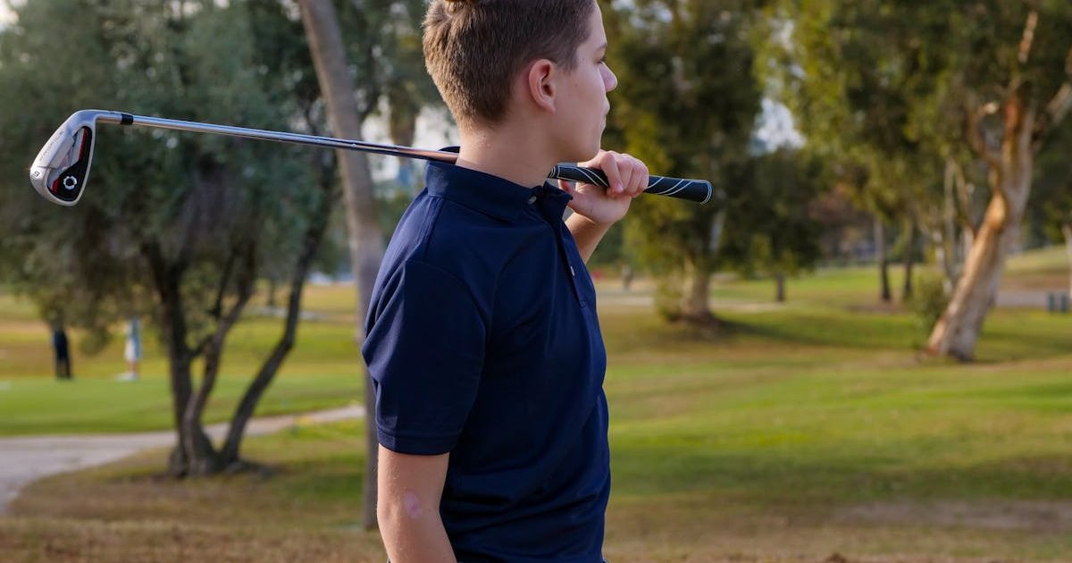 A teenage boy hitting a golf shot on a well-kept fairway on a bright day