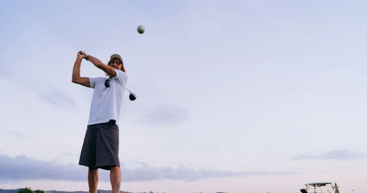 A golfer in a balanced follow-through against an evening sky, ball in flight