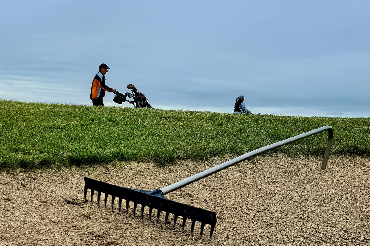 A golfer playing a bunker shot with an explosion of sand on a sunny golf course
