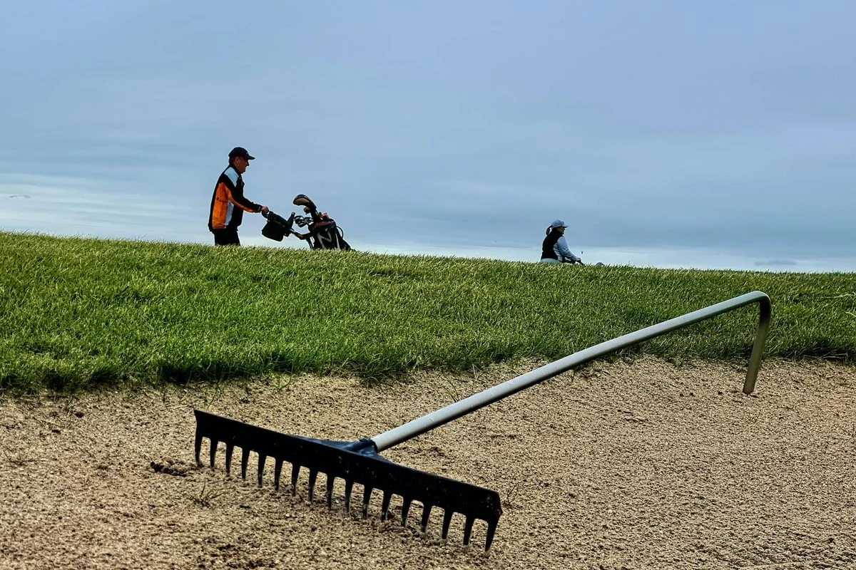 A golfer playing a bunker shot with an explosion of sand on a sunny golf course