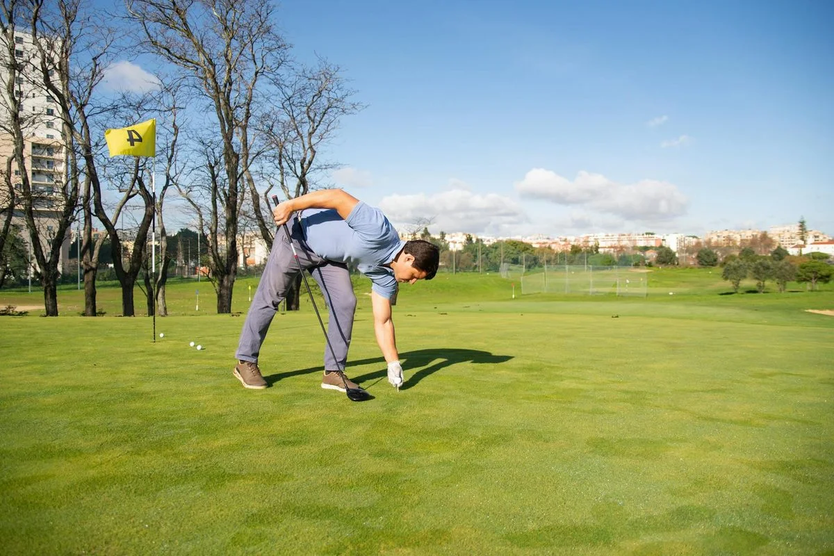 A golfer crouching behind a golf ball on the green, reading the putt towards the hole